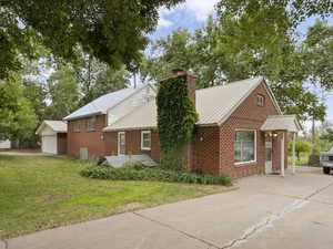 View of front of home with a chimney, brick siding, a metal roof, and driveway