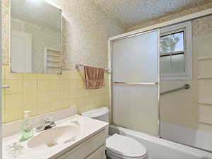 Full bathroom with shower / bath combination with glass door, wallpapered walls, vanity, and tile walls
