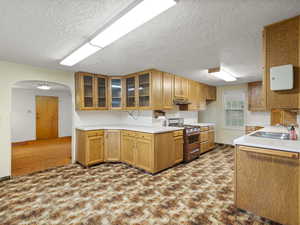Kitchen featuring light countertops, arched walkways, glass insert cabinets, gas range, and a textured ceiling