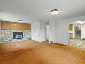 Unfurnished living room featuring stairway, a stone fireplace, carpet floors, a textured ceiling, and arched walkways