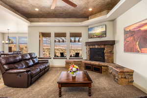Carpeted living room featuring a stone fireplace, a chandelier, and ceiling fan