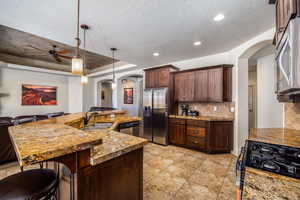 Kitchen with arched walkways, dark brown cabinetry, a breakfast bar area, appliances with stainless steel finishes, and decorative backsplash