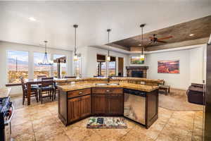 Kitchen with dark brown cabinetry, hanging light fixtures, stainless steel appliances, an island with sink, and a stone fireplace