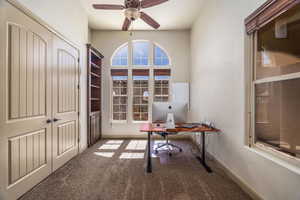 Carpeted home office featuring ceiling fan and baseboards, can also be a bedroom