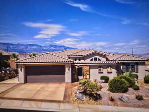 Mediterranean / spanish-style house with stucco siding, a mountain view, an attached garage, stone siding, and concrete driveway