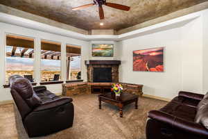 Living room with a stone fireplace, carpet, and a ceiling fan