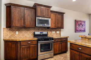 Kitchen featuring stainless steel appliances, backsplash, dark brown cabinets, light stone counters, and recessed lighting