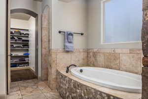 Bathroom with a bath, tile patterned flooring, a walk in closet, and a tile shower