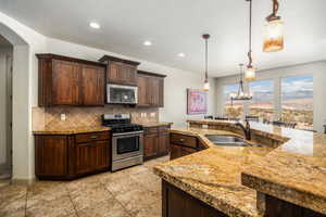 Kitchen featuring appliances with stainless steel finishes, a chandelier, tasteful backsplash, dark brown cabinets, and hanging light fixtures