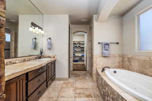 Full bath with vanity, a garden tub, a walk in closet, and light tile patterned floors