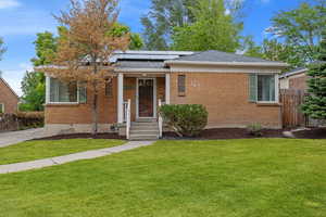 View of front of house featuring brick siding, solar panels, and a shingled roof