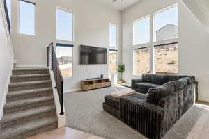 Living room with healthy amount of natural light, a high ceiling, stairs, light wood-style floors, and light carpet