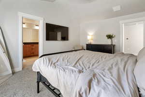 Bedroom featuring vaulted ceiling, ensuite bath, and light carpet