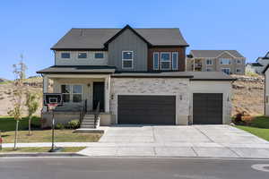 View of front facade with covered porch, concrete driveway, an attached garage, a front lawn, and stone siding