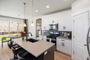 Kitchen with stainless steel appliances, a center island with sink, pendant lighting, white cabinets, and a kitchen breakfast bar