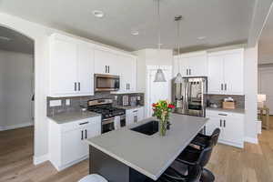Kitchen with a kitchen breakfast bar, appliances with stainless steel finishes, a kitchen island with sink, decorative light fixtures, and decorative backsplash