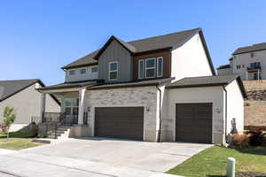 View of front facade featuring concrete driveway, a garage, stone siding, board and batten siding, and covered porch
