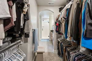 Walk in closet with arched walkways, light carpet, and light tile patterned floors