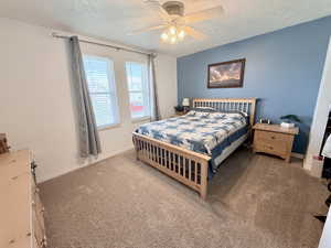 Bedroom with a textured ceiling, carpet floors, and a ceiling fan