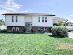 Bi-level home with brick siding, a front yard, and an attached carport