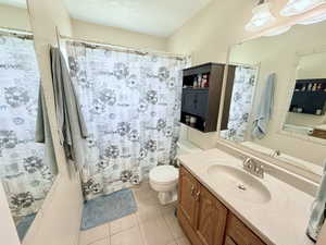 Full bath featuring a textured ceiling, light tile patterned flooring, vanity, and shower / bathtub combination with curtain