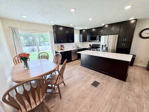 Kitchen with stainless steel appliances, a kitchen island, light wood finished floors, a textured ceiling, and light stone counters