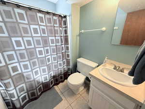 Bathroom with light tile patterned flooring, vanity, curtained shower, and a textured wall