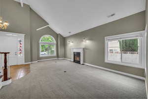 Unfurnished living room featuring high vaulted ceiling, carpet, tile patterned floors, a premium fireplace, and a chandelier