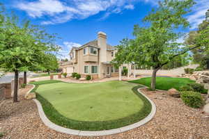 Back of property featuring a putting green, stucco siding, a chimney, a garage, and a patio