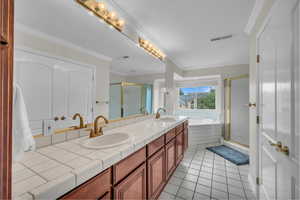 Full bath featuring ornamental molding, a stall shower, double vanity, light tile patterned floors, and a garden tub