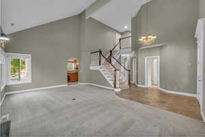 Unfurnished living room featuring a chandelier, light colored carpet, high vaulted ceiling, beam ceiling, and stairs