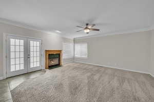 Unfurnished living room with french doors, crown molding, a fireplace, light carpet, and a textured ceiling