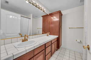 Bathroom featuring light tile patterned floors, double vanity, a textured ceiling, and a shower with shower curtain