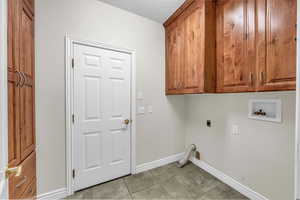 Laundry area with cabinet space, hookup for an electric dryer, light tile patterned floors, hookup for a washing machine, and a textured ceiling