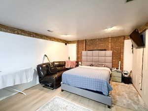 Bedroom featuring a textured ceiling, wood finished floors, and brick wall