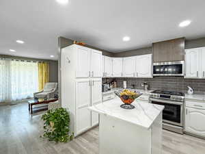 Kitchen with stainless steel appliances, backsplash, light wood finished floors, white cabinets, and light stone counters