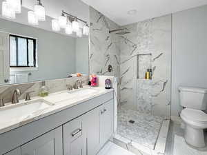 Bathroom featuring double vanity, a marble finish shower, and light tile patterned flooring