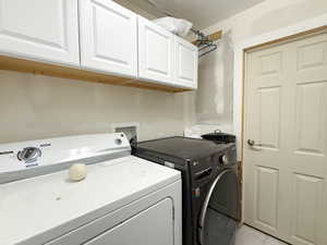 Laundry area with light tile patterned floors, cabinet space, and separate washer and dryer