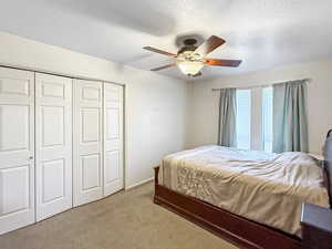 Carpeted bedroom with a closet, a textured ceiling, and a ceiling fan