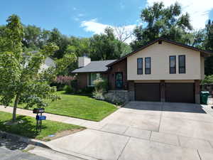 Tri-level home featuring brick siding, an attached garage, concrete driveway, a front yard, and a chimney
