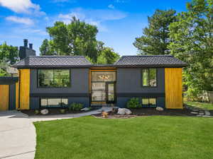 View of front of property featuring a front yard, a chimney, roof with shingles, and brick siding