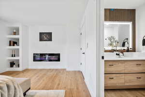 Master suite featuring light wood-style flooring, a glass covered fireplace, and built in shelves