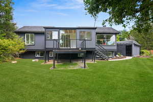 Rear view of house featuring a shingled roof, stairway, a wooden deck, a yard, and an outdoor structure