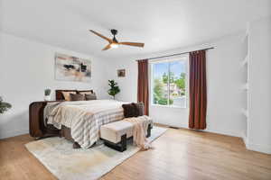 Master suite with light wood-style floors and a ceiling fan