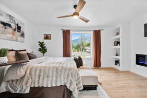 Master suite featuring light wood-style flooring, a glass covered fireplace, and a ceiling fan