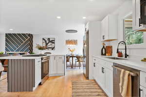 Kitchen with white cabinets, stainless steel appliances, light wood finished floors, a kitchen breakfast bar, and recessed lighting