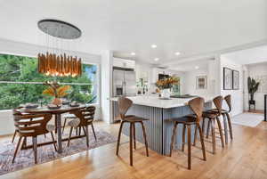 Kitchen featuring light wood finished floors, white cabinetry, recessed lighting, stainless steel refrigerator with ice dispenser, and a kitchen breakfast bar
