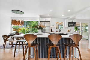 Kitchen with light wood finished floors, white cabinetry, recessed lighting, a kitchen bar, and stainless steel refrigerator with ice dispenser