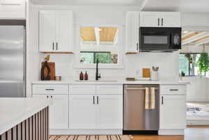 Kitchen featuring white cabinets, appliances with stainless steel finishes, light stone countertops, and light wood-style flooring