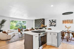 Kitchen with stainless steel gas range oven, open floor plan, light wood-style flooring, white cabinetry, and recessed lighting